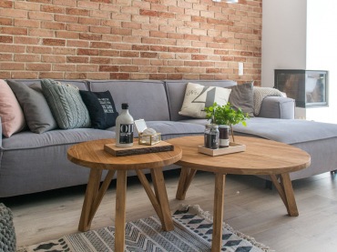Drewno oraz czerwone cegły to wyjątkowe materiały, które tworzą przytulny klimat w salonie. Dla kontrastu znajduje się tu szara sofa o prostym kształcie. Kominek potęguje wrażenie...