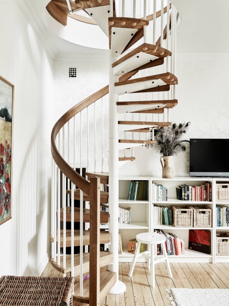 Spiralne kręcone schody w białym kolorze z drewnianymi stopniami w dwupoziomowym mieszkaniu
