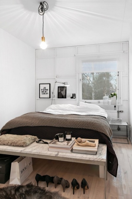 Żarówka na kablu,industrialne białe panele na ścianie,kamienna ławka ze szklanymi bokami i czarno-białe grafiki w skandynawskiej sypialni