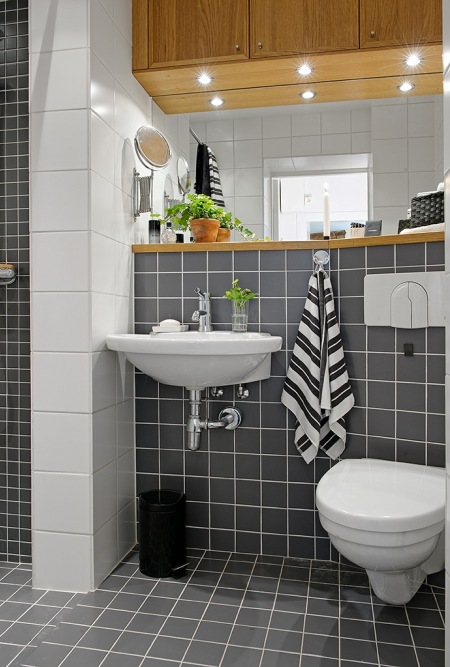 Czarne i białe kwadratowe płytki na scianie w małej łazience z drewnianymi półkami i szafkami