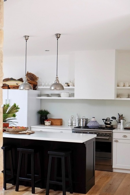Czarna wyspa kuchenna z białym blatem, srebrne metalowe lampy wiszące i półki zabudowane z białym okapem na ścianie w kuchni