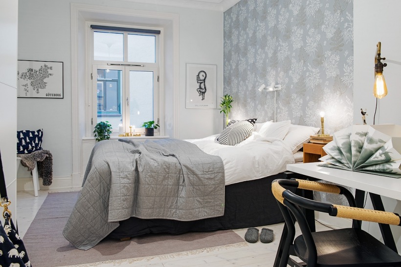 Szara pikowana narzuta na łóżko,biało-szara tapeta na ścianie,szary dywan,czarne łóżko i krzesło przy białym biurku w sypialni skandynawskiej