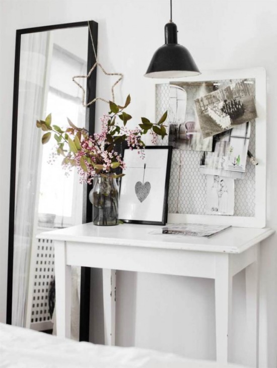 Prostokątne czarne lustro stojące,biały stolik z drewna,czarna lampa z metalu i dekoracje w przedpokoju