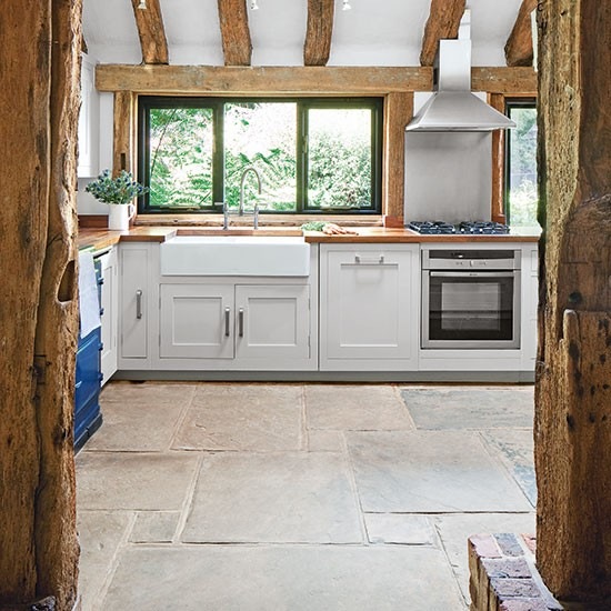 Skandynawska kuchnia w aranżacji wiejskiej kuchni z drewnianymi belkami i kamienną podłogą