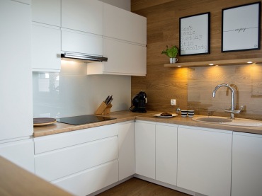 Białe szafki w kuchni w połączeniu z ciepłym drewnem wyznaczają skandynawski styl aranżacji. Minimalistyczne podejście do dekorowania przestrzeni sprawia, że pomieszczenie prezentuje się schludnie i świeżo. Typografia czy zioła w donicy w delikatny sposób urozmaicają...