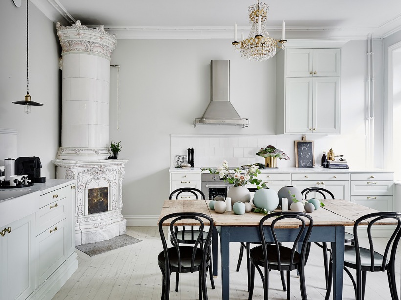Skandynawska kuchnia z ceramicznym piecem,kryształowym żyrandolem i szarym stołem z postarzanym blatem,krzesła giete z drewna w kuchni
