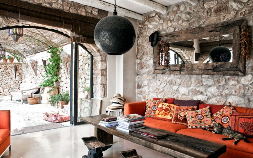 Kamienne ściany,drewniane lustro rustykalne,czarna lampa marokańska i czerwona kanapa z orientalnymi poduszkami