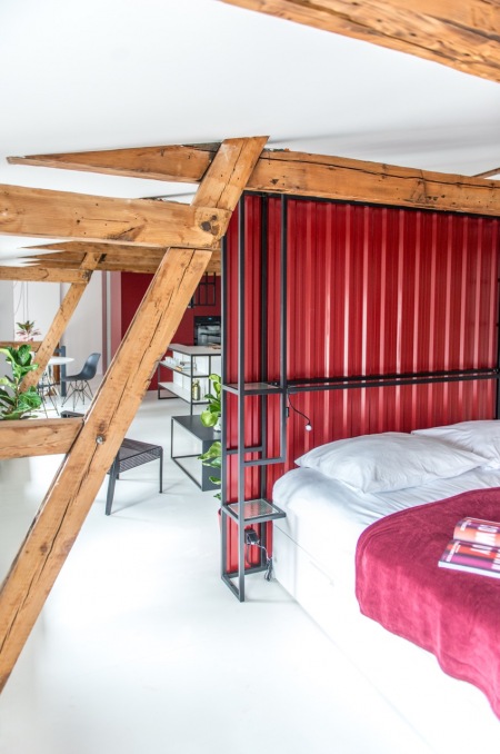 Sypialnia wydzielona w pokoju dziennym za pomocą czerwonej ścianki działowej