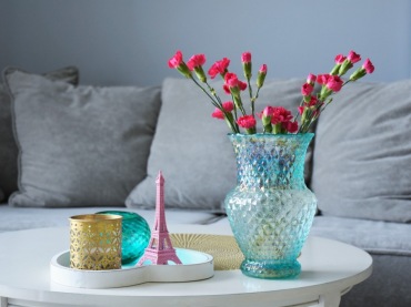 Na stoliku kawowym znajdują się dekoracje w paryskim klimacie. Drobne ozdóbki w różnych kolorach i bukiet kwiatów...