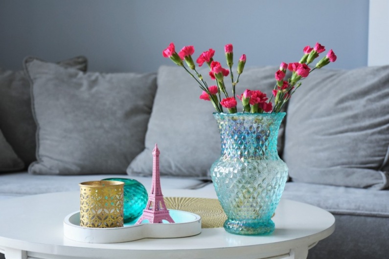 Na stoliku kawowym znajdują się dekoracje w paryskim klimacie. Drobne ozdóbki w różnych kolorach i bukiet kwiatów...