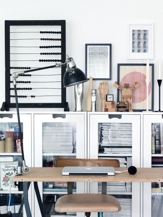 Białe przeszklone witryny na podłodze,metalowe biurko z drewnianym blatem,industrialne krzesło biurkowe i czarna lamka przypieta do blatu biurka