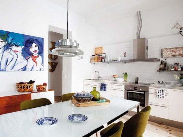 Jasna drewniana podłogo w białej nowoczesnej kuchni  to świetne rozwiązanie.Zielone krzesła i obraz wprowadzają...