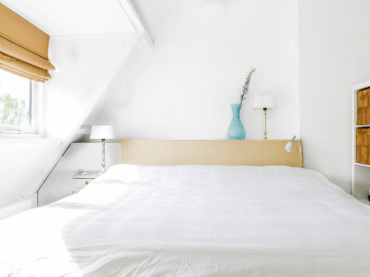 Ogromne łóżko w sypialni urządzonej w stylu skandynawskim zapewni odpowiednią dawkę komfortu po ciężkim dniu. Biel...
