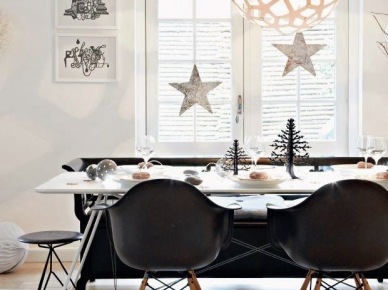 Czarne nowoczesne krzesła muszle i metalowy taboret przy skandynawskim stole świątecznym z wiszącymi białymi gwiazdkami i czarnymi małymi choinkami (27435)