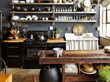 Prawdziwa kuchnia z duszą, otwarte półeczki, czarna kuchenka i drewniany stół na tle szarej ściany wygląda...