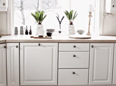 Białe szafki rozświetlają kuchenną przestrzeń, podobnie jak jasna podłoga czy większość dodatków. Drewniany blat...