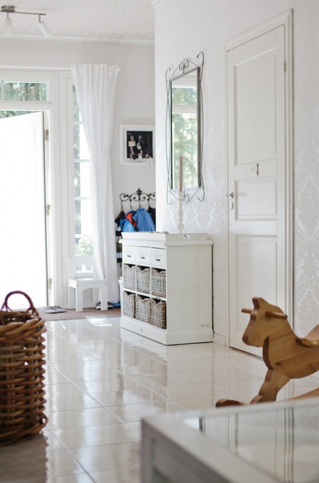 Biała komoda z drewna i wiklinowymi koszykami pod kutym lustrem na ścianie