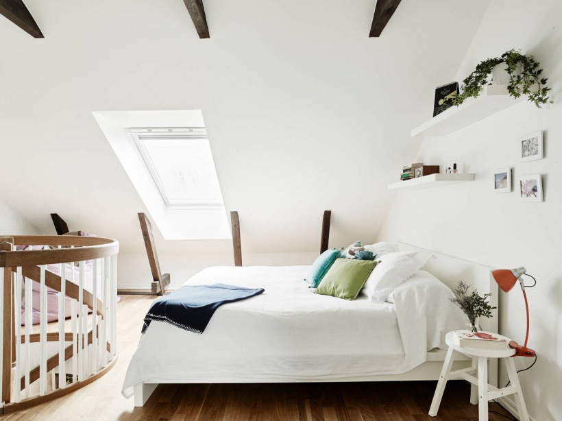 Biała sypialnia w stylu skandynawskim  ze skośnym sufitem z drewnianymi belkami i półokragłą balustradą przy schodach
