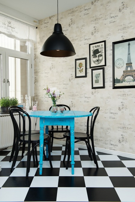 Tapeta ścienna z napisami w stylu vintage,czarna lampa pendant,czarne krzesła z gietego drewna,niebieski okrągły stół i biało-czarna terakota ułożona w szachownicę w kuchni