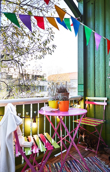Kolorowa aranżacja małego balkonu z różowym stolikiem i proporczykami