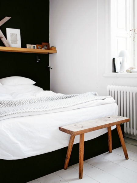 Czarna ściana z łóżkiem i drewniana połka w białej sypialni