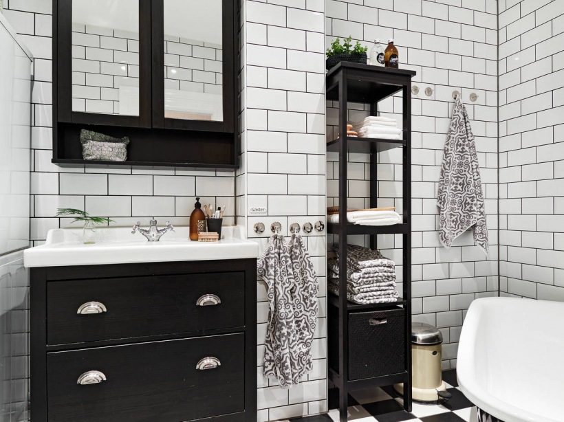 Biała glazura cegiełka na ścianie w łazience, posadzka w szachownicę ,wolnostojąca czarna wanna i czarne etażerki z półkami w małej łazience