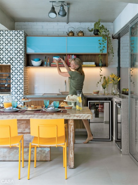 Niebieskie szafki w kuchni w połączeniu zdrewnem i żółtymi krzesłami w jadalni