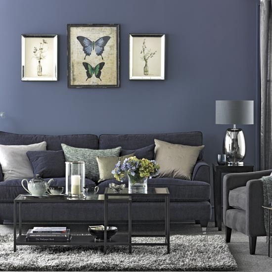Ciemno-niebieska ściana w salonie z szarą sofą,, metalowymi kwadratowymi stolikami i chromoniklowanymi detalami
