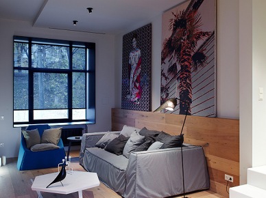 Nowoczesne artprinty na ścianach , niebieski fotel i sześciokątny biały stolik w  salonie (23756)
