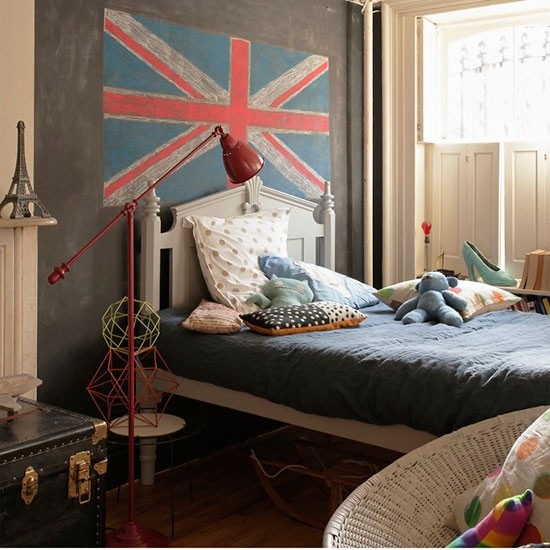 Drewniane łóżko, czerwona lampa,kufer i ściana w tablicowym kolorze