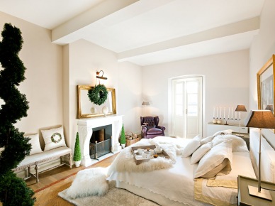 Przestronna sypialnia z kominkiem urządzona jest w klasycznym stylu. Eleganckie wykończenie i takie elementy jak lustro w złoconej ramie wypełniają subtelnie przestrzeń. Świąteczny wieniec i zielone drzewka delikatnie podkreślają grudniową...