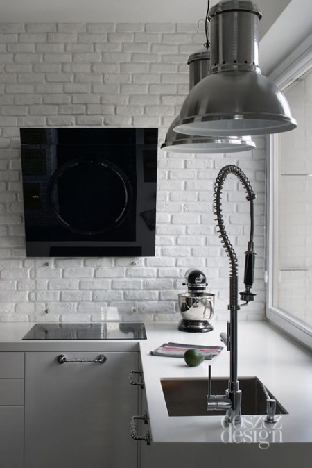 Biała cegła na ścianie,szare lampy pendant i nowoczesny okap w kuchni