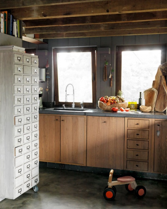 Drewniane belki w szarej kuchni z drewnianymi frontami,biała komoda wysoka z szufladkami i betonowa podłoga