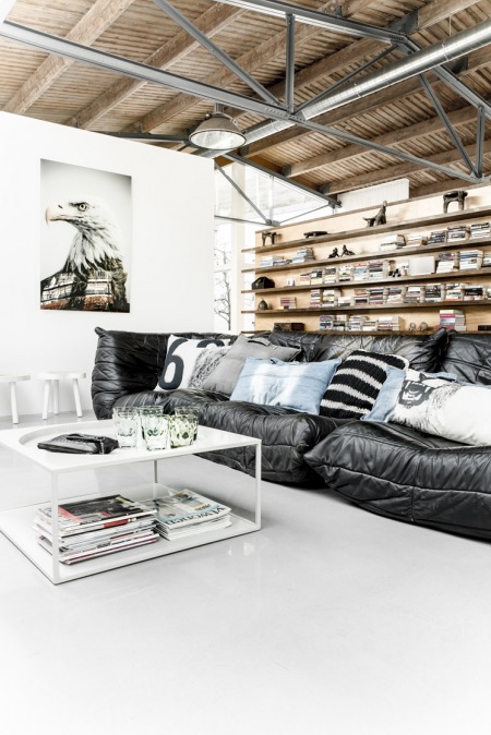 Pikowana nowoczesna sofa,drewniane półki z książkami i biały metalowy stolik kawowy