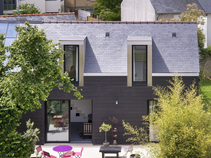 Mały domek w skandynawskim stylu z czarną elewacja i wąskim oknami typu lukarny