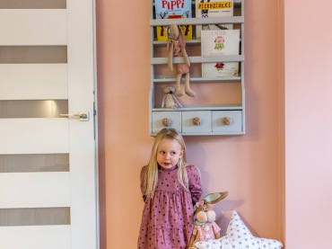 W pokoju dziecięcym jedna ze ścian pomalowano na różowy pudrowy kolor. Na niej zawieszono wąską półeczkę z praktycznymi...