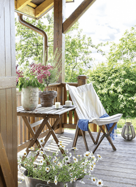 Drewniany stolik na krzyżaku i drewniany fotel skandynawski z białym płótnem,lampiony i rustykalne osłonki na kwiaty na wiejskiej werandzie