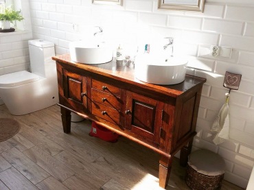 Aranżacja białej łazienki z drewnianą podłogą i rzeźbioną szafką. Dwie umywalki zapewniają wygodny równoległy dostęp...