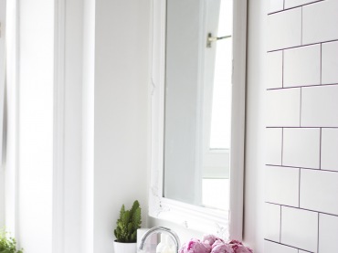 Dekoracyne, białe lustro nad umywalką nadaje aranżacji uroku, dodatkowo podkreślonego różowymi kwaitami w szklanym...