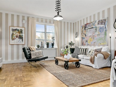 Skandynawski salon z tapetą w beżowe pasy,z biała sofą, jutowym dywanem, czarną lampą i stolikiem na kólkach w stylu industrialnym (27684)