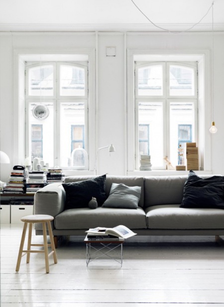 Szara kanapa z czarnymi poduszkami w białym salonie