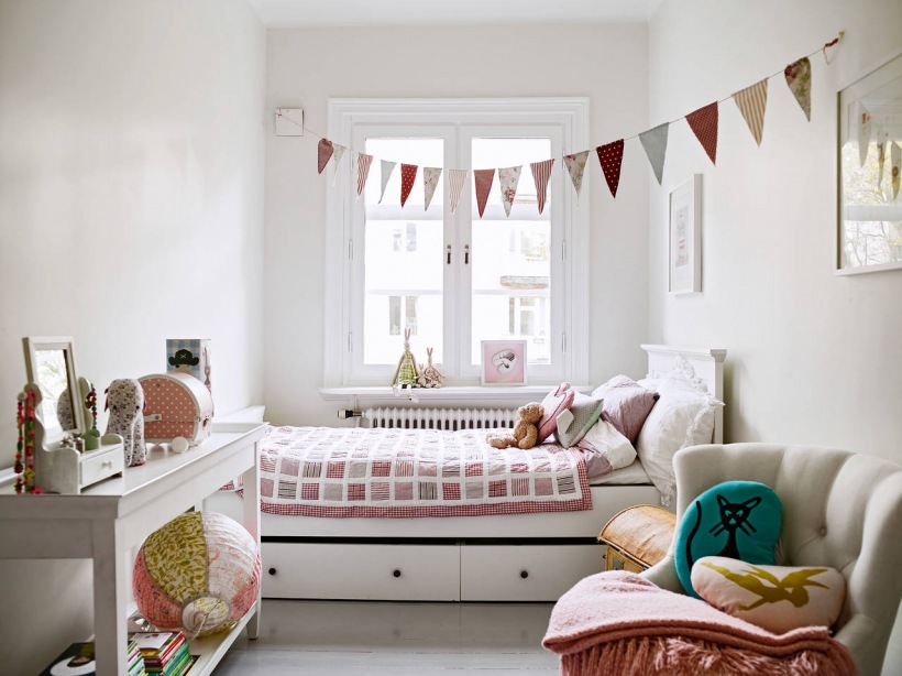 Girlanda z kolorowych proporczyków w pokoju dziecięcym , łóżko z szufladami,biała konsolka i pikowany foteli w stylu angielskim