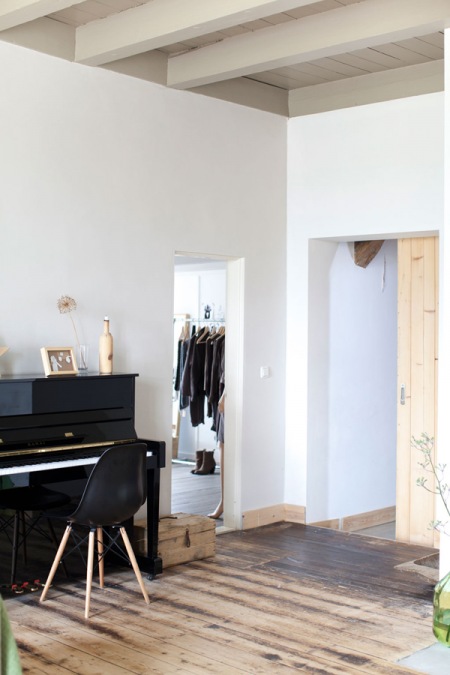 Szary sufit z desek,biale ściany i ciemna drewniana podłoga w salonie z pianinem