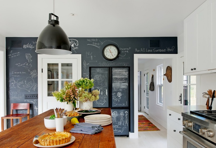 Czarna ściana w kuchni pomalowana farbą tablicową,czarna lampa industrialna,biała kuchnia i drewniany blat stołu