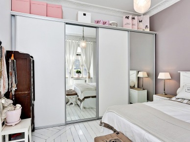 Biała szafa z przesuwnymi lustrzanymi drzwiami i różowe pudełka w aranżacji skandynawskiej sypialni (24389)