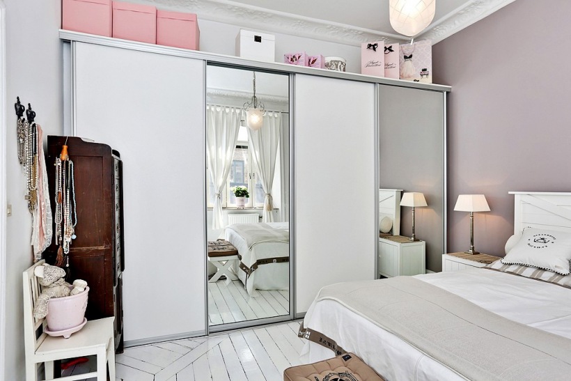 Biała szafa z przesuwnymi lustrzanymi drzwiami i różowe pudełka w aranżacji skandynawskiej sypialni