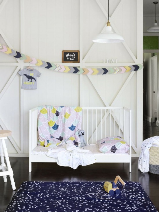 Białe łóżeczko,pastelowa girlanda i pościel w dzieciecym pokoju z białymi panelami na ścianie