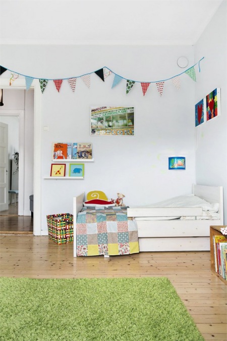 Kolorowa girlanda z proporczykami w dziecięcym pokoju z białymi ścianami i narzutą patchwork na łóżku