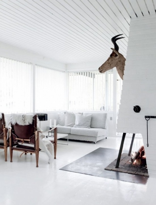 Biały salon skandynawski z kominkiem,brązową głową renifera i brązowymi fotelami