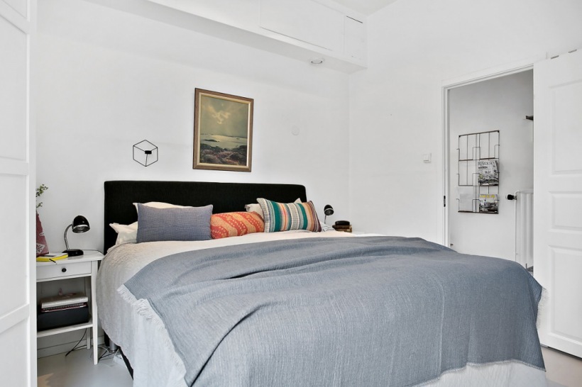 Szara narzuta,czarne tapicerowane łóżko,białe stoliki nocne i obraz retro na białej ścianie w sypialni